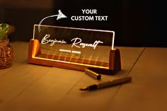 an illuminated business card holder with a pen next to it on a wooden table top