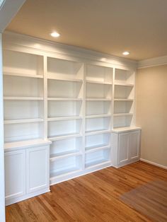 an empty room with white bookcases and wood floors