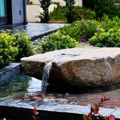 a large rock sitting in the middle of a garden with water coming out of it