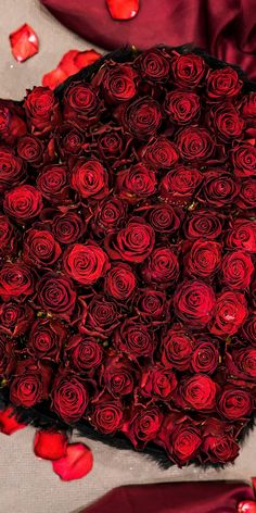 a large bouquet of red roses sitting on top of a table with petals scattered around it