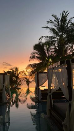 the sun is setting over an outdoor swimming pool with white drapes and palm trees