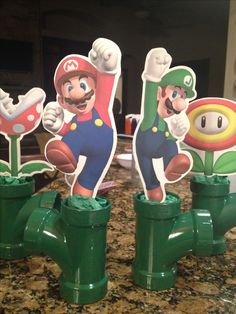 some paper cutouts are sitting on top of green pipe holders in the shape of mario and luigi