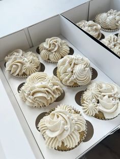 cupcakes with white frosting sitting in a box on display at a bakery