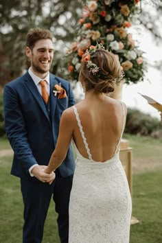 a bride and groom hold hands as they stand in front of an outdoor ceremony arch