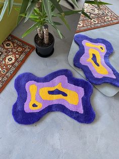 two purple and yellow rugs sitting on top of a floor next to a potted plant