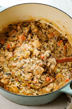 a pot filled with chicken and vegetables on top of a table next to a wooden spoon