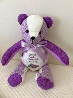 a purple and white teddy bear sitting on top of a bed next to a wall