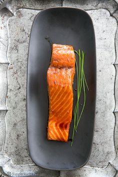 a piece of salmon sitting on top of a black plate