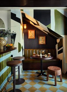 the interior of a restaurant with tables and stools in front of a painted wall