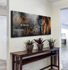 a wall hanging above a wooden table with two planters on it and a sign that says, let your faith be bigger than your fear