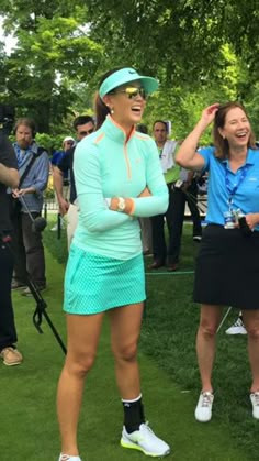 two women standing on top of a lush green field next to each other holding golf racquets