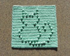 a crocheted square with small green flowers on it, sitting on the ground