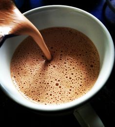 a person stirring hot chocolate in a white cup