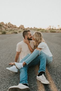 a man and woman are sitting on the road together, one is kissing his forehead