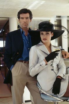 a man standing next to a woman in a white coat and black hat on top of a chair