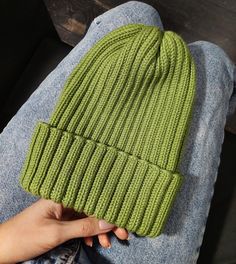 a person is holding up a green knitted beanie on their lap, while sitting down