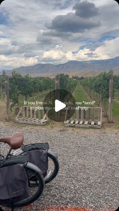 a bicycle parked on the side of a gravel road next to a wooden fence and vineyard