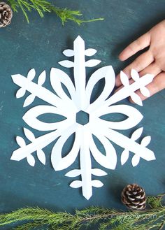 someone is making a paper snowflake ornament with pine cones and evergreen branches