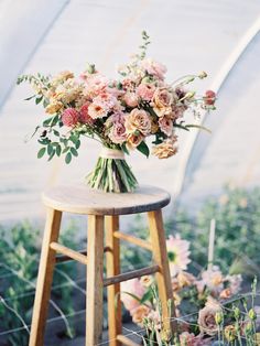 a bouquet of flowers sitting on top of a wooden stool in a greenhouse filled with plants