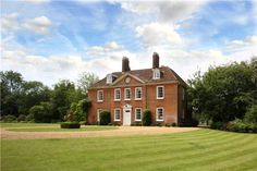 a large red brick house sitting in the middle of a lush green field with lots of trees