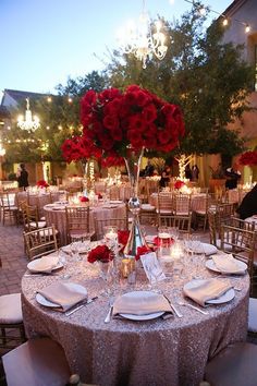 the tables are set with red roses and silverware for an elegant wedding reception at night