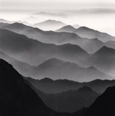 black and white photograph of mountains with fog in the air, taken from top of a mountain