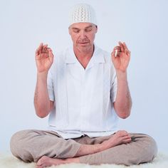 an older man sitting in the middle of a meditation pose with his hands up and eyes closed