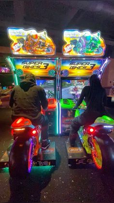 two people on motorcycles playing video games in a room with neon lights and arcade machines