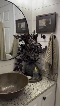 a bathroom sink sitting under a round mirror next to a vase with flowers in it