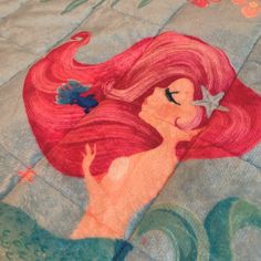 the little mermaid has pink hair and is holding a starfish in her hand while sitting on top of a quilt