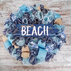 a wreath with the word beach written on it and blue ribbon around it, sitting on top of a wooden table