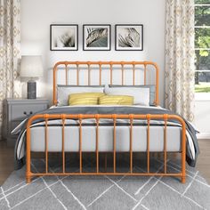 an orange metal bed frame in a bedroom with two pictures on the wall above it