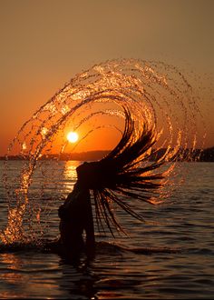 a woman is standing in the water with her hair blowing back and sun setting behind her