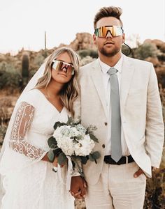 a bride and groom pose for a photo in front of the desert with their sunglasses on