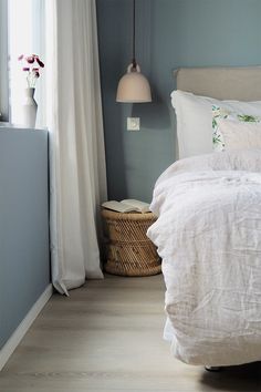 a white bed sitting in a bedroom next to a window with curtains on the side