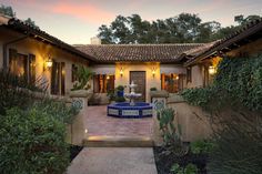 an outdoor courtyard with a fountain surrounded by greenery and plants at dusk or dawn