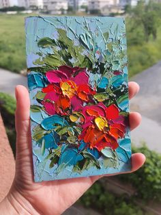 a person holding up a piece of art with flowers painted on it's side