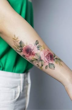 a woman's arm with pink flowers on it and leaves around the wrist tattoo