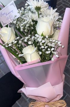 a bouquet of white roses and baby's breath wrapped in pink paper