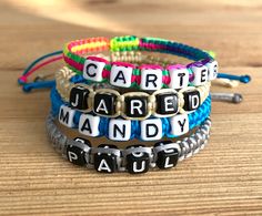 four bracelets with words on them sitting on a wooden table next to a screw