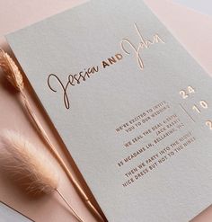 a wedding card with a feather resting on it's side next to a pen