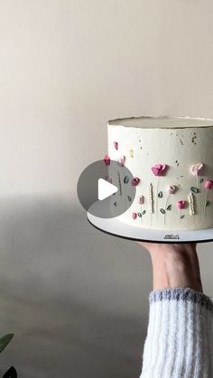 a person holding a white cake with pink flowers on it and an arrow in the middle