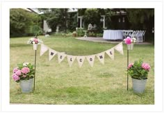 two buckets filled with flowers sitting on top of a grass covered field next to a welcome sign