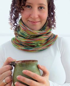 a woman with curly hair holding a cup in front of her face and wearing a scarf around her neck