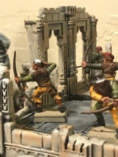 some toy soldiers are playing with each other in front of a gate and building that is made out of clay