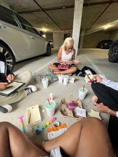 three people sitting on the ground in front of a car with papers, pens and markers