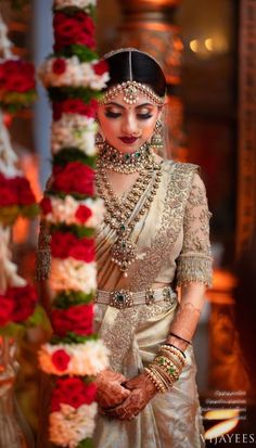 a woman in a wedding outfit standing next to red and white flowered garlands