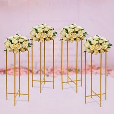 four gold stands with white roses in them on a pink background and one is holding a bouquet