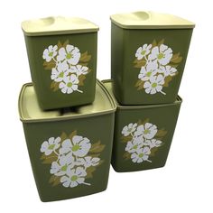 three green containers with white flowers painted on them