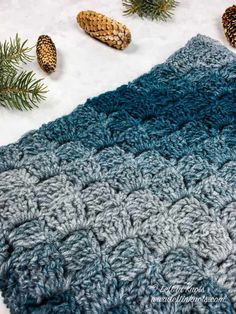 a crocheted blanket with pine cones on it and evergreen needles in the background